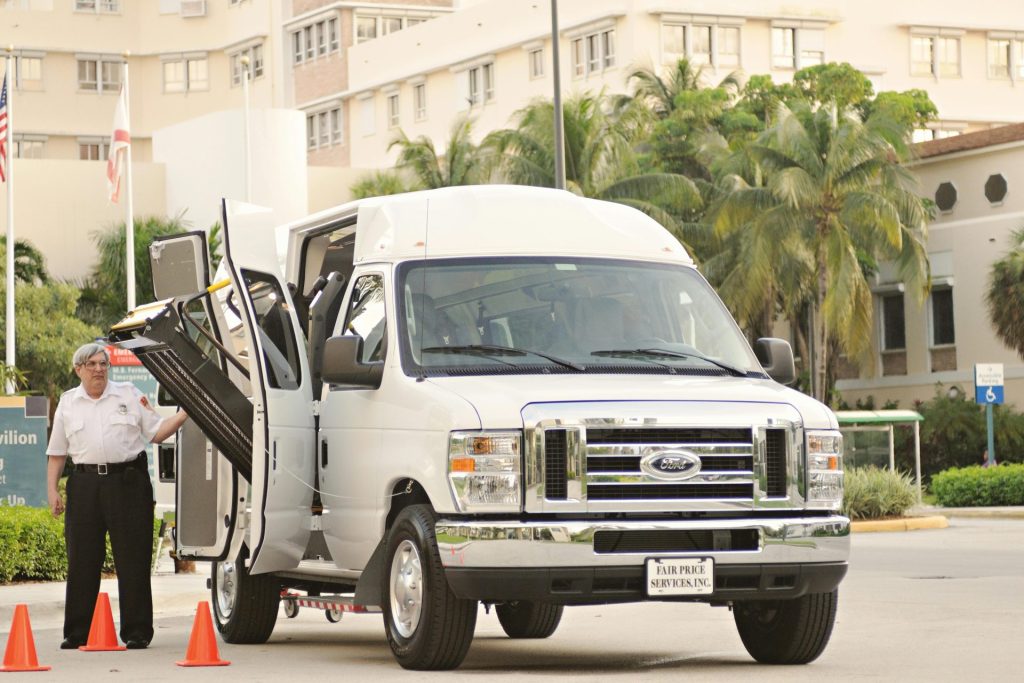 White passenger van with a deployed lift, parked near modern urban buildings.